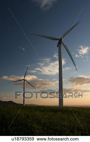 Stock Photo - view of wind turbines, on grassy hill, in Southern Italy at sunset, against blue sky. Fotosearch