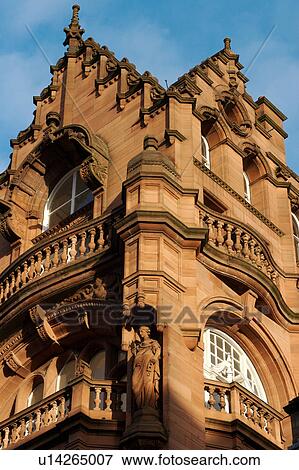 Stock Photo - view upwards of ornate stone corner of Victorian building, with balustrades, carvings, arched windows, against blue sky, central Glasgow, Scotland. Fotosearch