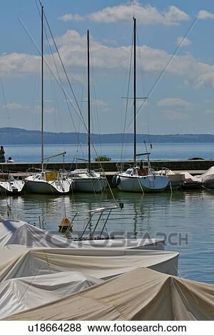 Yachts in harbour, with jetty beyond, blue sky, mountains and calm water on sunny summer day, Lake Trasimeno, Umbria, Italy View Large Photo Image Stock Photo - Yachts in harbour, with jetty beyond, blue sky, mountains and calm water on sunny summer day, Lake Trasimeno, Umbria, Italy. Fotosearch