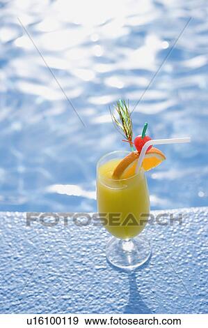 Stock Photo - Close-up of a glass of orange juice on the ledge of a swimming pool. Fotosearch