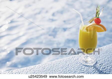 Stock Photo - Close-up of a glass of orange juice on the ledge of a swimming pool. Fotosearch