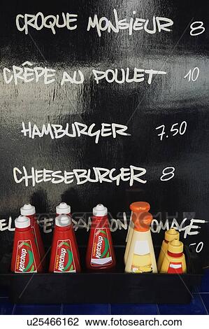 Stock Image - Close-up of tomato ketchup bottles in front of menu list on a blackboard. Fotosearch