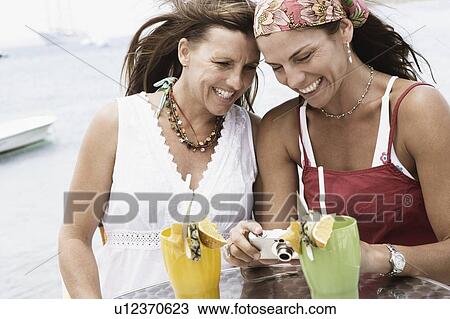 Stock Image - Close-up of two mid adult women looking at a digital camera and smiling. Fotosearch