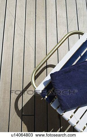 Stock Image - High angle view of a lounge chair and a towel on a floorboard. Fotosearch