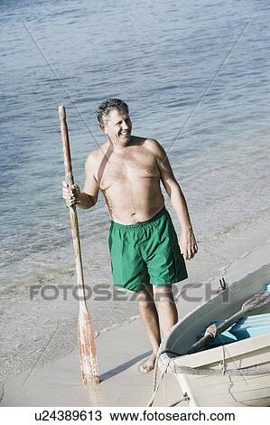 Stock Image - High angle view of a senior man holding an oar on the beach. Fotosearch