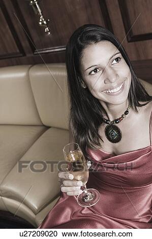 Stock Image - High angle view of a young woman holding a champagne flute and smiling. Fotosearch