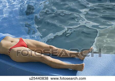 Stock Photo - Low section view of a woman lying on the ledge of a swimming pool. Fotosearch