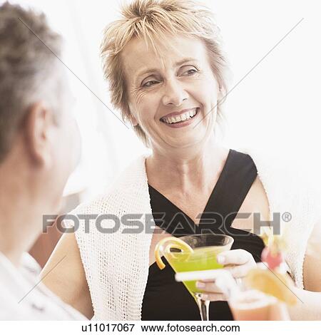 Stock Photo - Mature woman and a senior man holding glasses of cocktail and smiling. Fotosearch