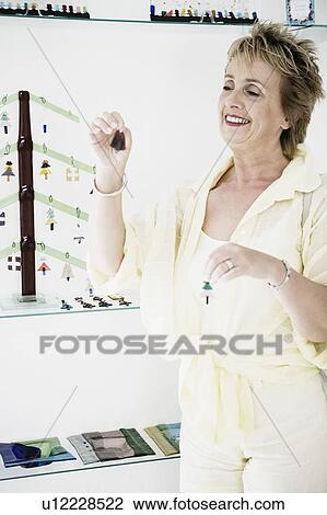 Stock Image - Mature woman choosing earrings. Fotosearch