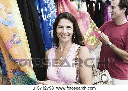 Stock Photo - Mid adult couple looking clothes at a market stall. Fotosearch