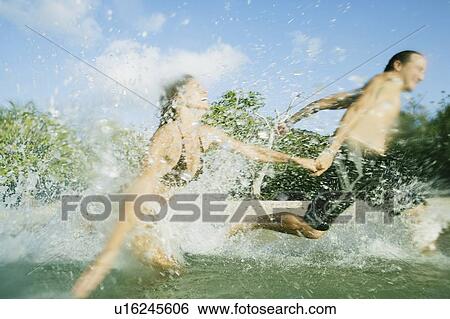 Mid adult couple running in water on the beach View Large Photo Image Stock Photograph - Mid adult couple running in water on the beach. Fotosearch