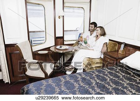 Stock Photography - Mid adult couple sitting in a cabin of a sailing ship and holding glasses of cocktail. Fotosearch