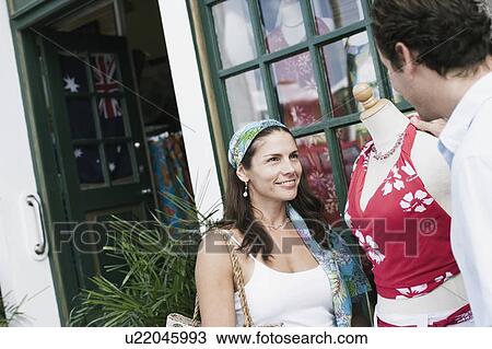 Stock Image - Mid adult couple standing near a mannequin outside a store and smiling. Fotosearch