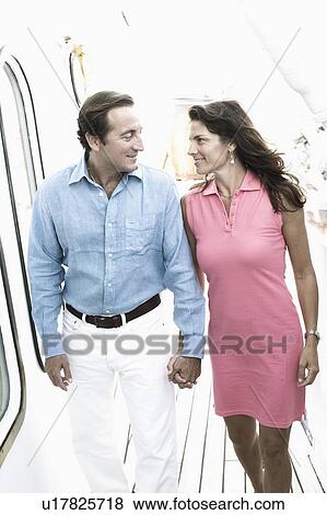 Mid adult couple walking with holding hands of each other on the deck of a cruise ship and looking at each other View Large Photo Image Stock Photo - Mid adult couple walking with holding hands of each other on the deck of a cruise ship and looking at each other. Fotosearch