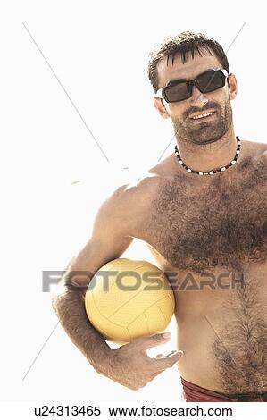Stock Photography - Mid adult man holding a beach volleyball on the beach. Fotosearch