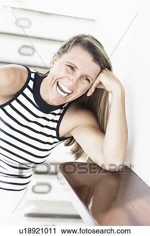 Stock Image - Mid adult woman laughing with her head in her hand. Fotosearch