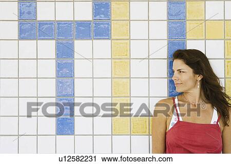 Stock Image - Mid adult woman leaning against a tiled wall. Fotosearch