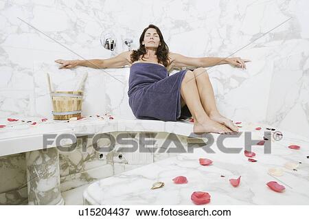 Stock Photo - Mid adult woman sitting in the bathroom. Fotosearch