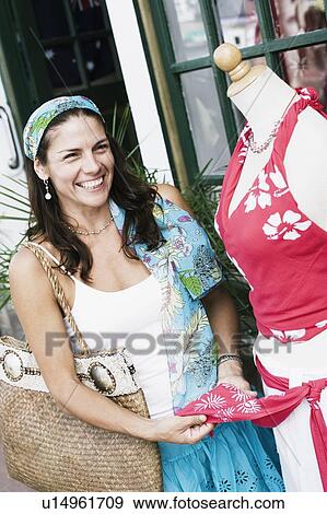 Stock Photo - Mid adult woman standing near a mannequin outside a store and smiling. Fotosearch