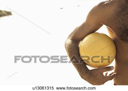 Stock Photography - Mid section view of a man holding a beach volleyball on the beach. Fotosearch