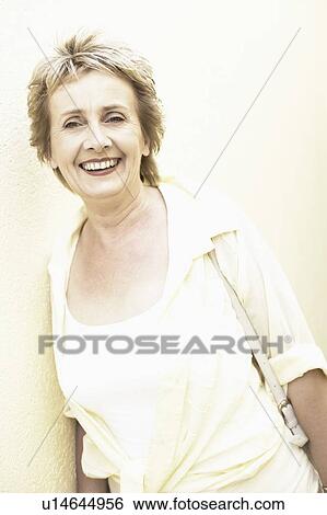 Stock Photograph - Portrait of a mature woman leaning against a wall and smiling. Fotosearch