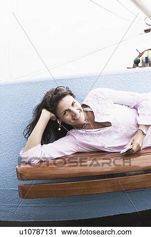 Portrait of a mid adult woman lying on a bench and listening to an MP3 player View Large Photo Image Stock Image - Portrait of a mid adult woman lying on a bench and listening to an MP3 player. Fotosearch