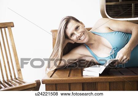 Stock Photo - Portrait of a mid adult woman lying on a bench and holding a book. Fotosearch