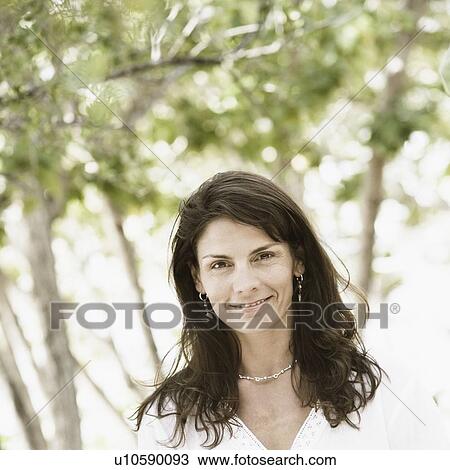 Stock Image - Portrait of a mid adult woman standing on the beach and smiling. Fotosearch