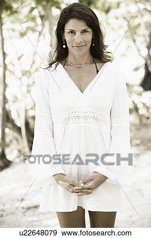 Stock Photo - Portrait of a mid adult woman standing with her hands clasped on the beach. Fotosearch