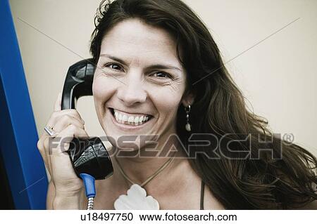Stock Image - Portrait of a mid adult woman talking on a pay phone. Fotosearch