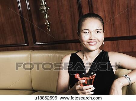 Portrait of a young woman holding a glass of martini and smiling View Large Photo Image Stock Photograph - Portrait of a young woman holding a glass of martini and smiling. Fotosearch