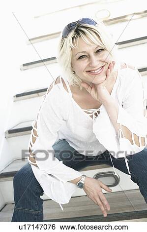 Stock Photograph - Portrait of a young woman sitting on steps with her hands on her chin and smiling. Fotosearch