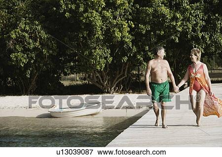 Stock Photo - Senior man and a mature woman holding each other's hands and walking on a jetty. Fotosearch