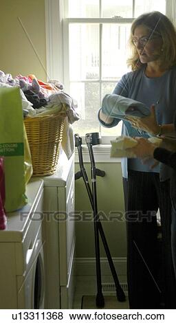 A woman folding cloths leaves her arm crutches leaning against the window. View Large Photo Image Stock Photo - A woman folding cloths leaves her arm crutches leaning against the window.. Fotosearch