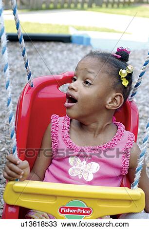 Stock Image - Adorable little girl with multiple disabilities having a great time swinging at the playground.. Fotosearch