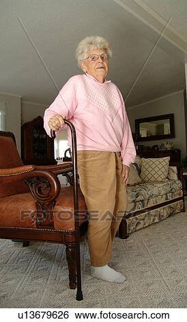 Stock Photograph - An elderly woman gets up from a break in her living room.. Fotosearch
