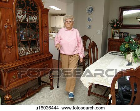 An elderly woman walks through her dining room to another room in her house. View Large Photo Image Picture - An elderly woman walks through her dining room to another room in her house.. Fotosearch