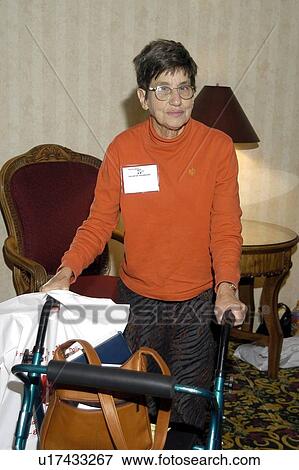Stock Photo - Elderly woman using a walker to carry her purse as she walks through a building.. Fotosearch
