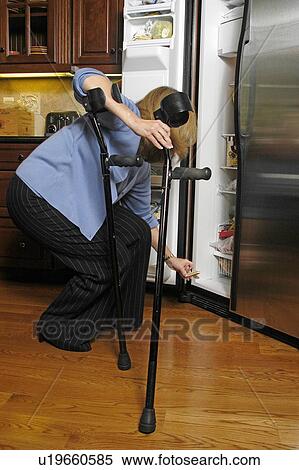 Stock Photography - Female with arm crutches gets food out of her refrigerator.. Fotosearch