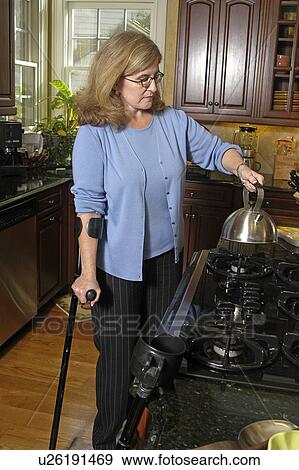 Stock Photo - Female with arm crutches prepares the morning coffee.. Fotosearch