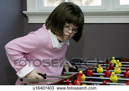 Stock Image - Little girl with Down syndrome playing foosball.. Fotosearch