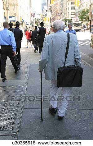 Stock Photograph - Man using a cane for walking stability on a city street.. Fotosearch