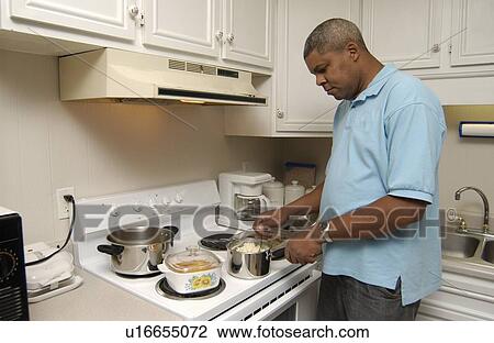 Stock Image - Man with a disability cooking his dinner in his kitchen, in his own apartment.. Fotosearch