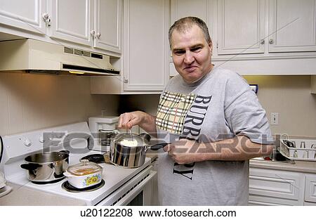 Stock Photo - Man with a disability cooking his dinner in his kitchen, in his own apartment.. Fotosearch