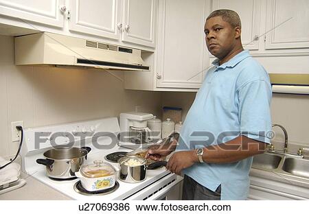 Stock Photograph - Man with a disability cooking his dinner in his kitchen, in his own apartment.. Fotosearch