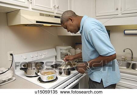 Stock Photography - Man with a disability cooking his dinner in his kitchen, in his own apartment.. Fotosearch