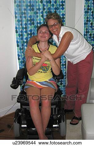 Picture - Mother hugs daughter (electric wheelchair user) and smiles for the camera.. Fotosearch
