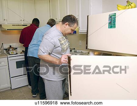 Stock Photo - Three men with disabilities preparing a meal in the home they share.. Fotosearch