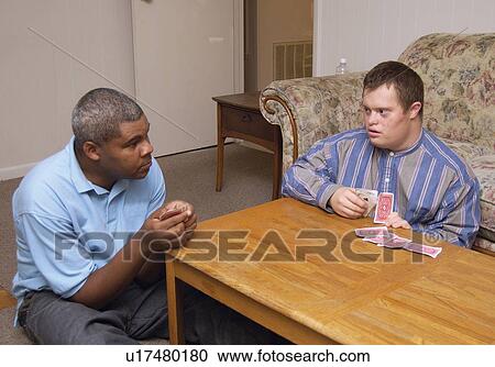 Stock Image - Two men with disabilities playing a game of cards in the living room in their home.. Fotosearch