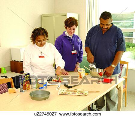 Stock Photo - Two people with disabilities learning to prepare meals from recipes with the assistance of a staff person.. Fotosearch